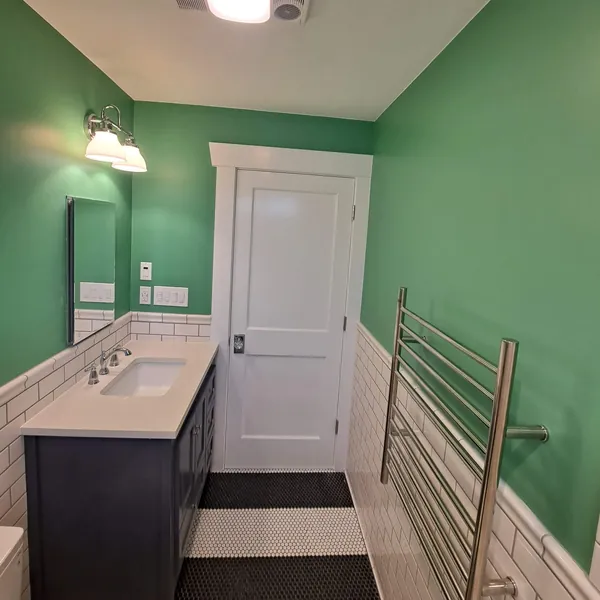 Bathroom with green walls, a navy vanity, white subway-tile wainscot and a striped black-and-white penny-tile floor