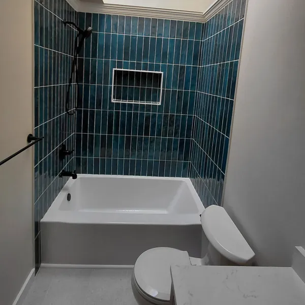 Tub and shower in glossy teal vertical tile with a niche, black fixtures and a skylight above