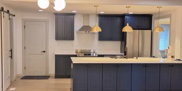 Open kitchen with navy shaker cabinets, a long island with brass pendant lights and a white sliding barn door