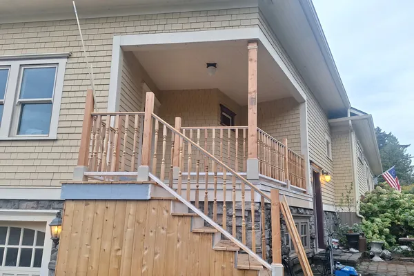 Finished front porch with new turned-baluster railings and stairs down to the driveway, with the stone skirting below